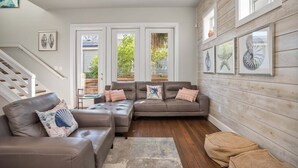 A living room with a brown leather sectional sofa, a small round table, and a staircase. - The Oyster House - Pet Friendly! Golf Cart Included! (Port Aransas)
