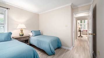 A bedroom with two beds, a nightstand, a lamp, and a door leading to another room.