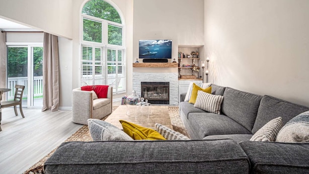 Sala de estar con chimenea, televisor y vista a la vegetación a través de amplios ventanales.
