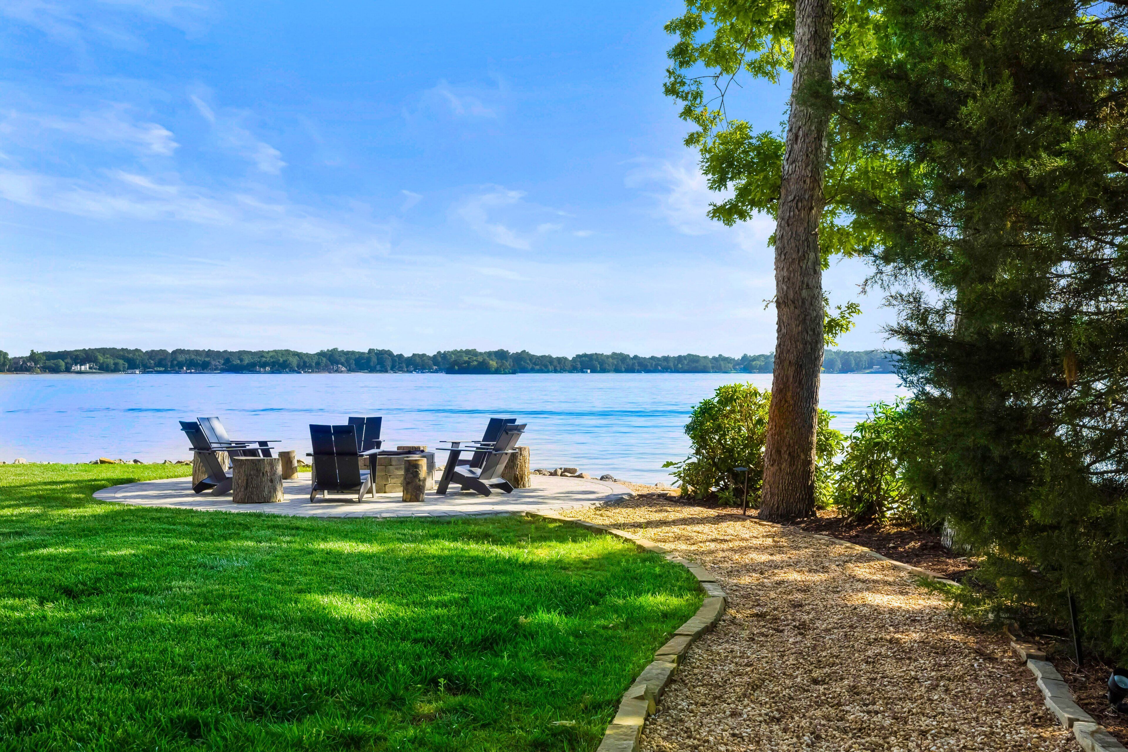 Une terrasse meublée, donnant sur un lac, entourée de verdure et sous un ciel dégagé.