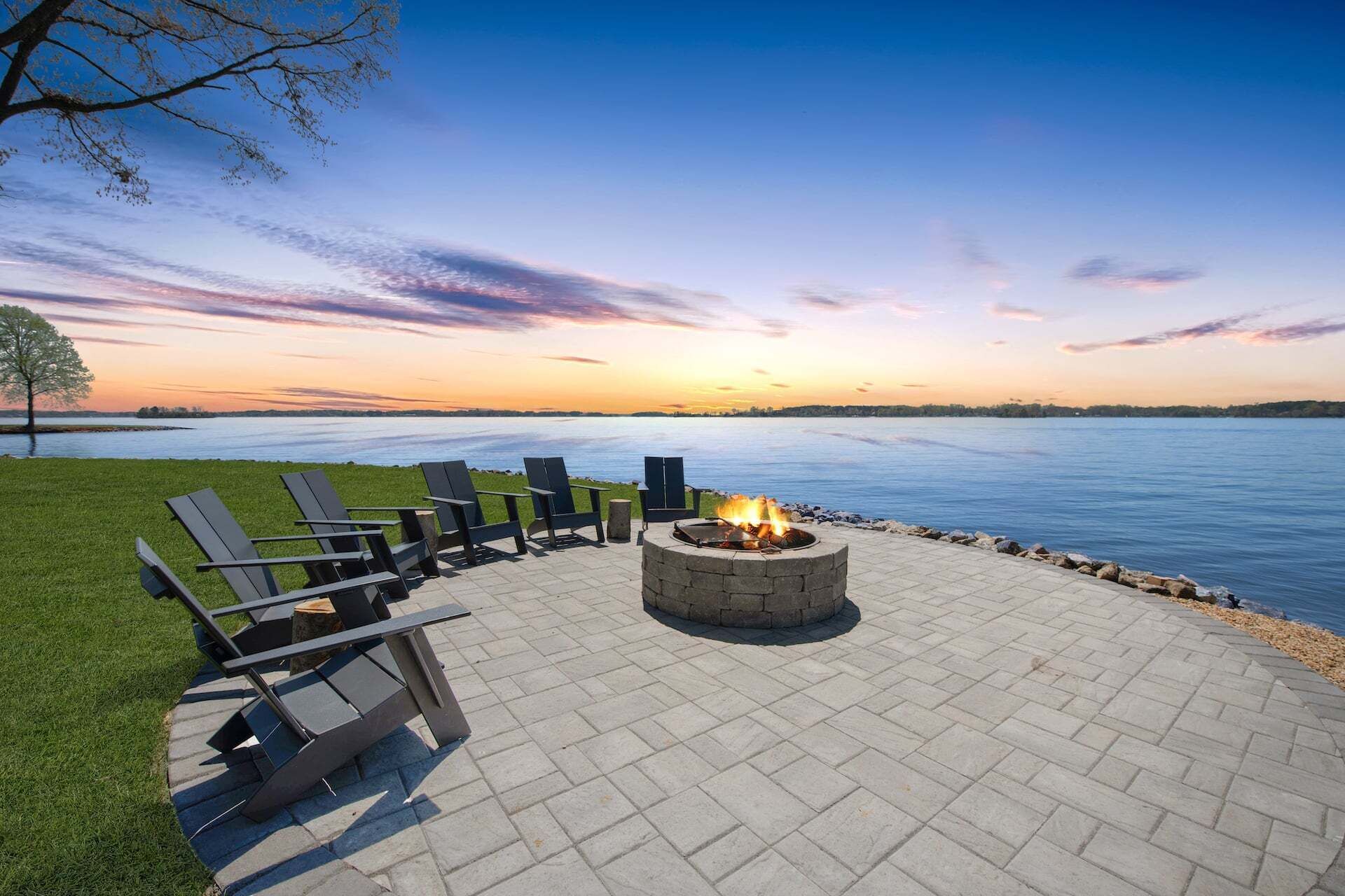 A fire pit with chairs and a view of a lake at sunset.