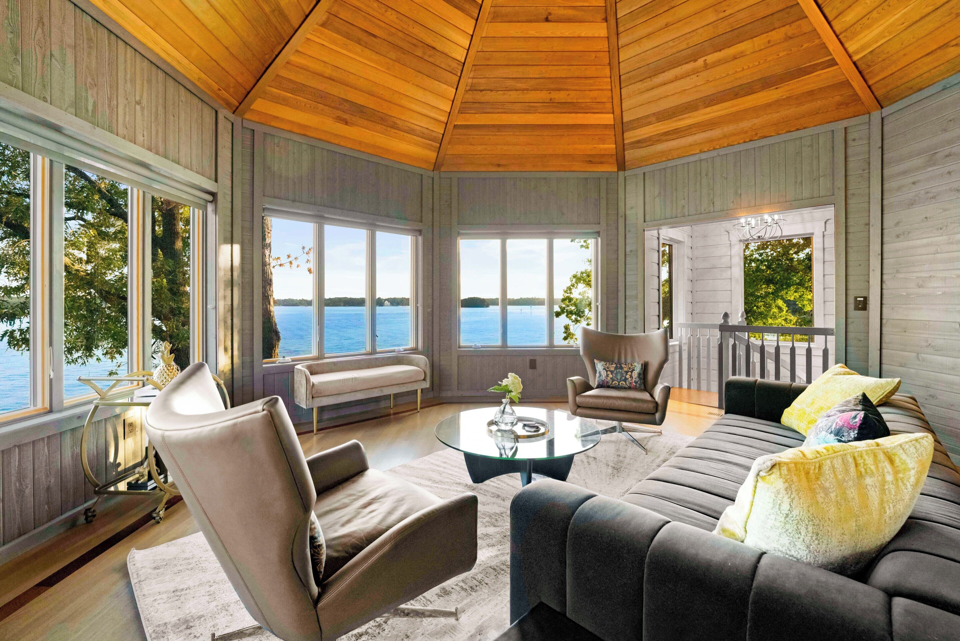 A spacious room with large windows, a wooden ceiling, and a cozy seating area with a sofa and chairs.