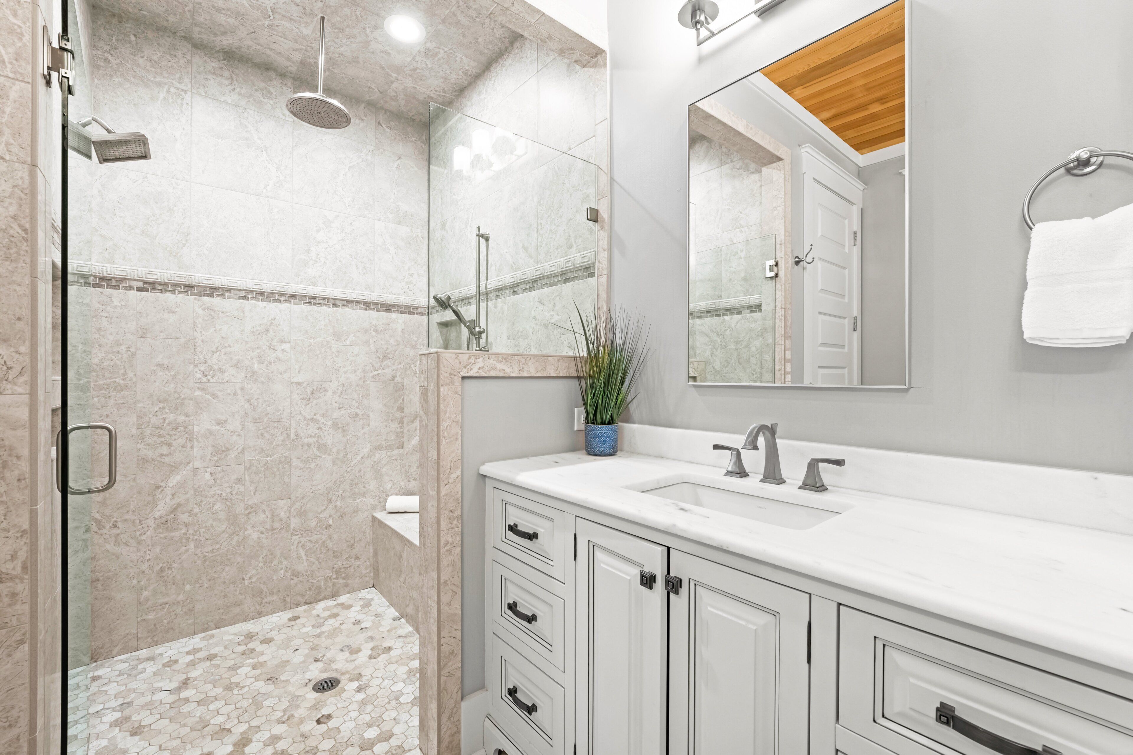 Une salle de bain moderne avec une douche à parois de verre, un grand miroir et un meuble-lavabo blanc doté de tiroirs.