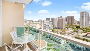 A balcony with a glass table and chairs, overlooking a cityscape with high-rise buildings and a road. - Stunning Ala Moana 2501 (Honolulu)