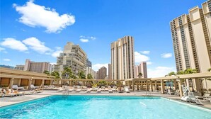 A swimming pool area with lounge chairs and umbrellas, surrounded by tall buildings. - Stunning Ala Moana 2501 (Honolulu)