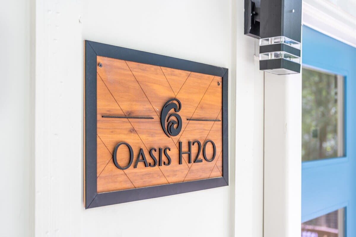 A wooden sign with the text "OASIS H2O" mounted on a wall.
