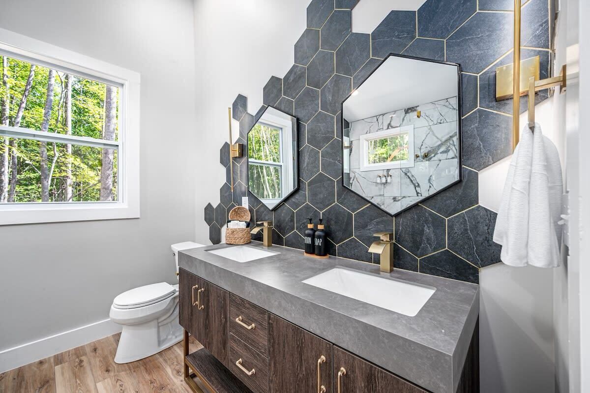 Une salle de bain moderne avec deux lavabos, des toilettes et une fenêtre donnant sur des arbres.