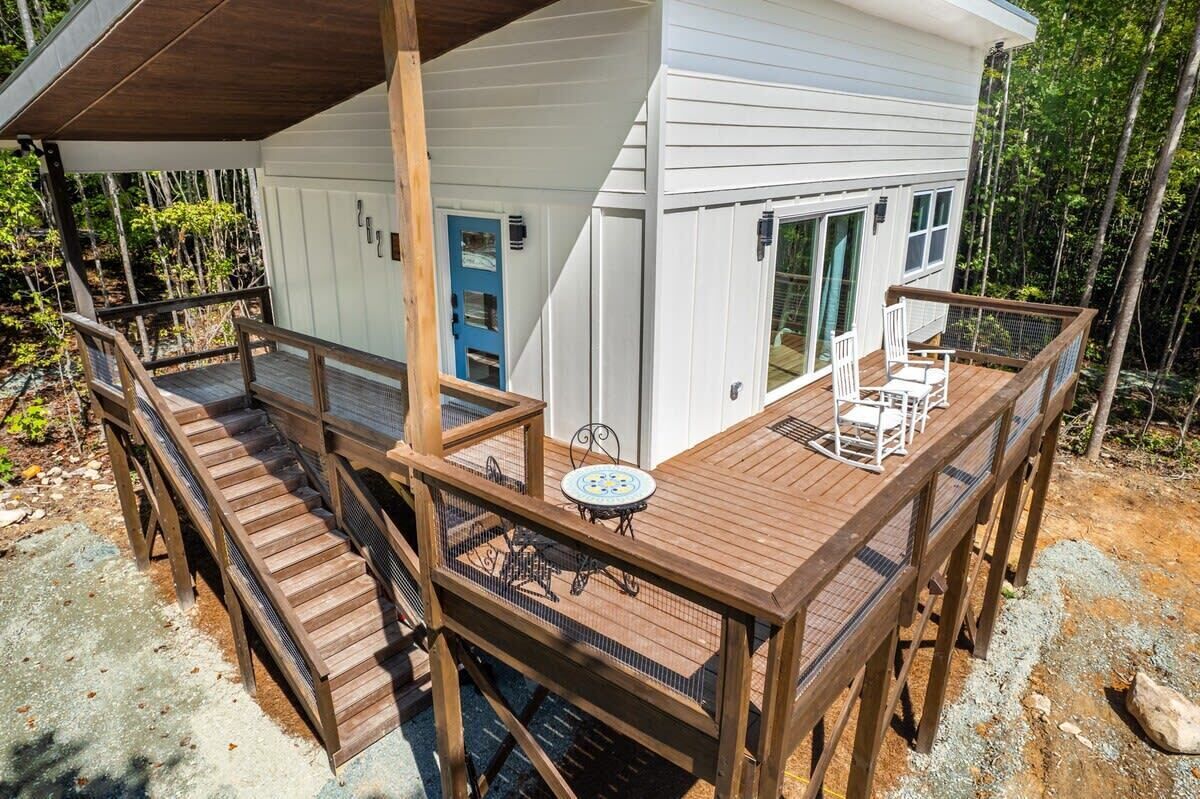 A wooden deck with a table and chairs, a blue door, and a white building with large windows.