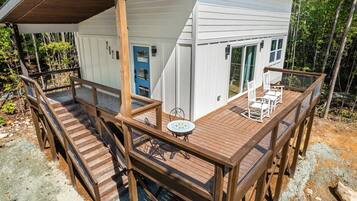 A wooden deck with a table and chairs, a blue door, and a white building with large windows.