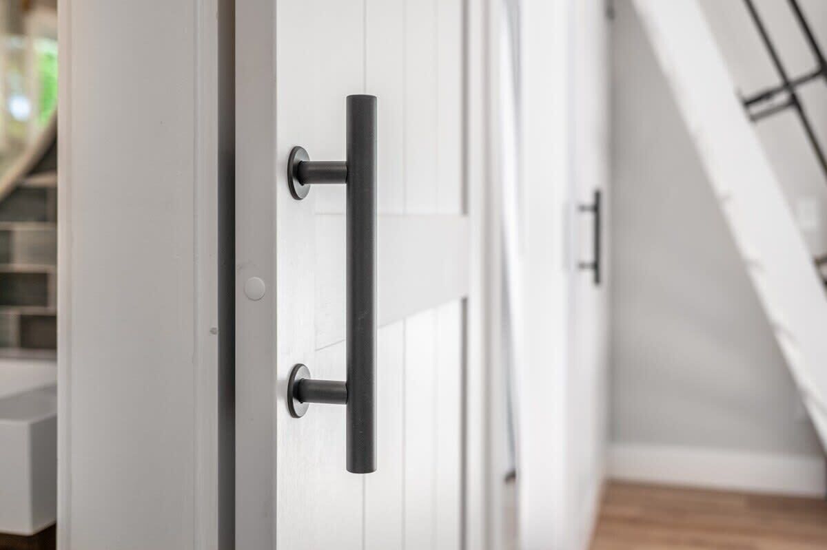 A white door with a black handle and a keyhole, part of a room with white walls and a wooden floor.