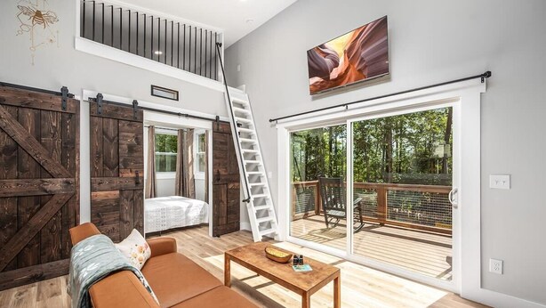A modern living room with a sofa, coffee table, and a view of a deck. - Two Tree Houses - Beehive & H20 (Pittsboro)