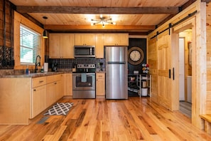 A modern kitchen with wooden cabinets, stainless steel appliances, and a wooden floor.