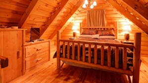 A cozy attic bedroom with a wooden bed, a nightstand, a dresser, and a chandelier. - Hot Tub & Wifi - Hidden Chalet Red River Gorge, KY (Campton)