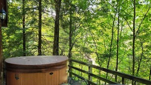 A hot tub on a wooden deck with a metal chair and a wooden railing overlooking a forest. - Hot Tub & Wifi - Hidden Chalet Red River Gorge, KY (Campton)