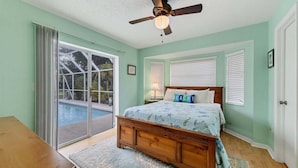 Un dormitorio con cama, ventilador de techo y vistas a una piscina a través de un ventanal corredera.