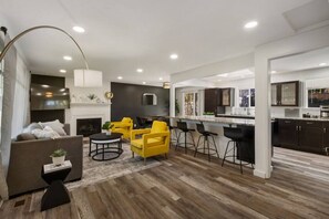 Uma sala de estar moderna com lareira, cadeiras amarelas e uma área de cozinha com banquetas.