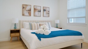 Ein ordentlich eingerichtetes Schlafzimmer mit einem großen Bett, zwei Nachttischen und drei abstrakten Bildern an der Wand.