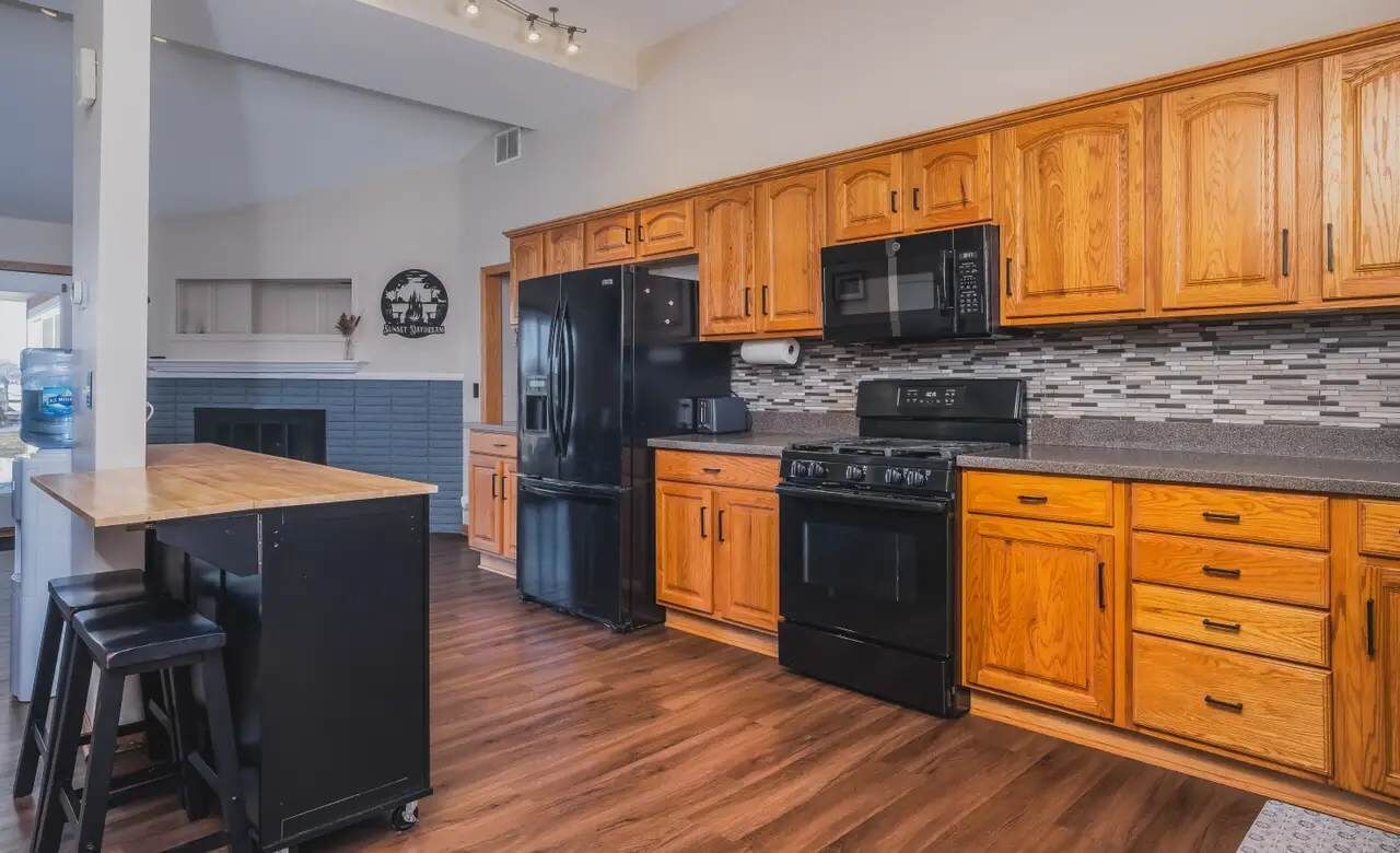 A modern kitchen with wooden cabinets, a black refrigerator, a microwave, and a stove.