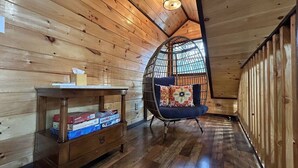 A wooden interior with a high ceiling, a wicker chair with cushions, and a small wooden table with boxes. - Wifi & Hot Tub, Large Family - Climb On in Rrg! (Rogers)