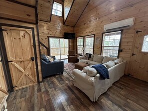 Een gezellig chaletinterieur met houten wanden, een grote bank, een blauwe fauteuil en een houten deur.