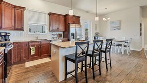 A modern kitchen with wooden cabinets, a central island, bar stools, and a dining area with a white table and chairs. - Mtd10333 (Port Charlotte)