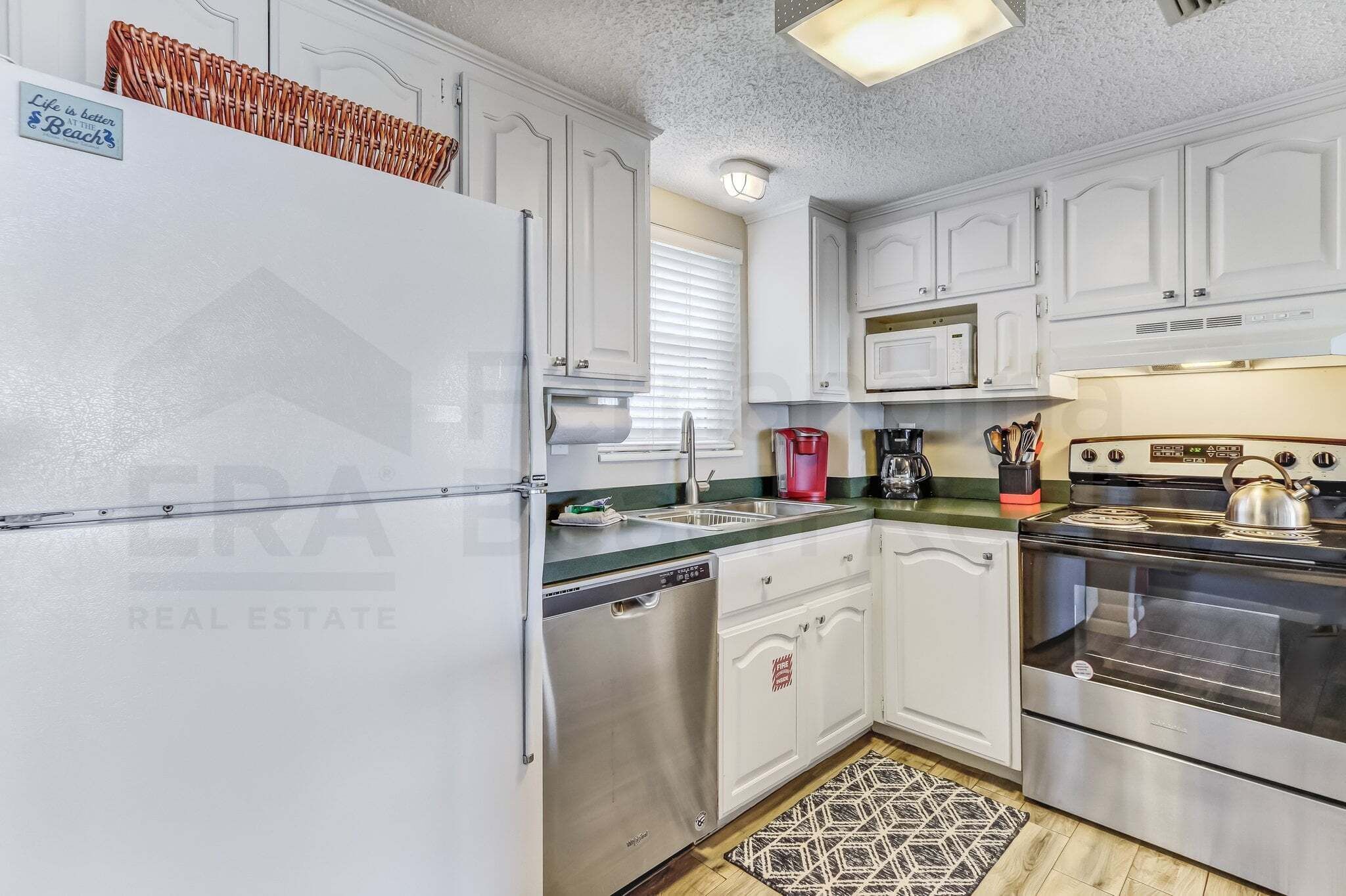 A kitchen with white cabinets, a stainless steel refrigerator, a dishwasher, a microwave, a stove, and a sink.