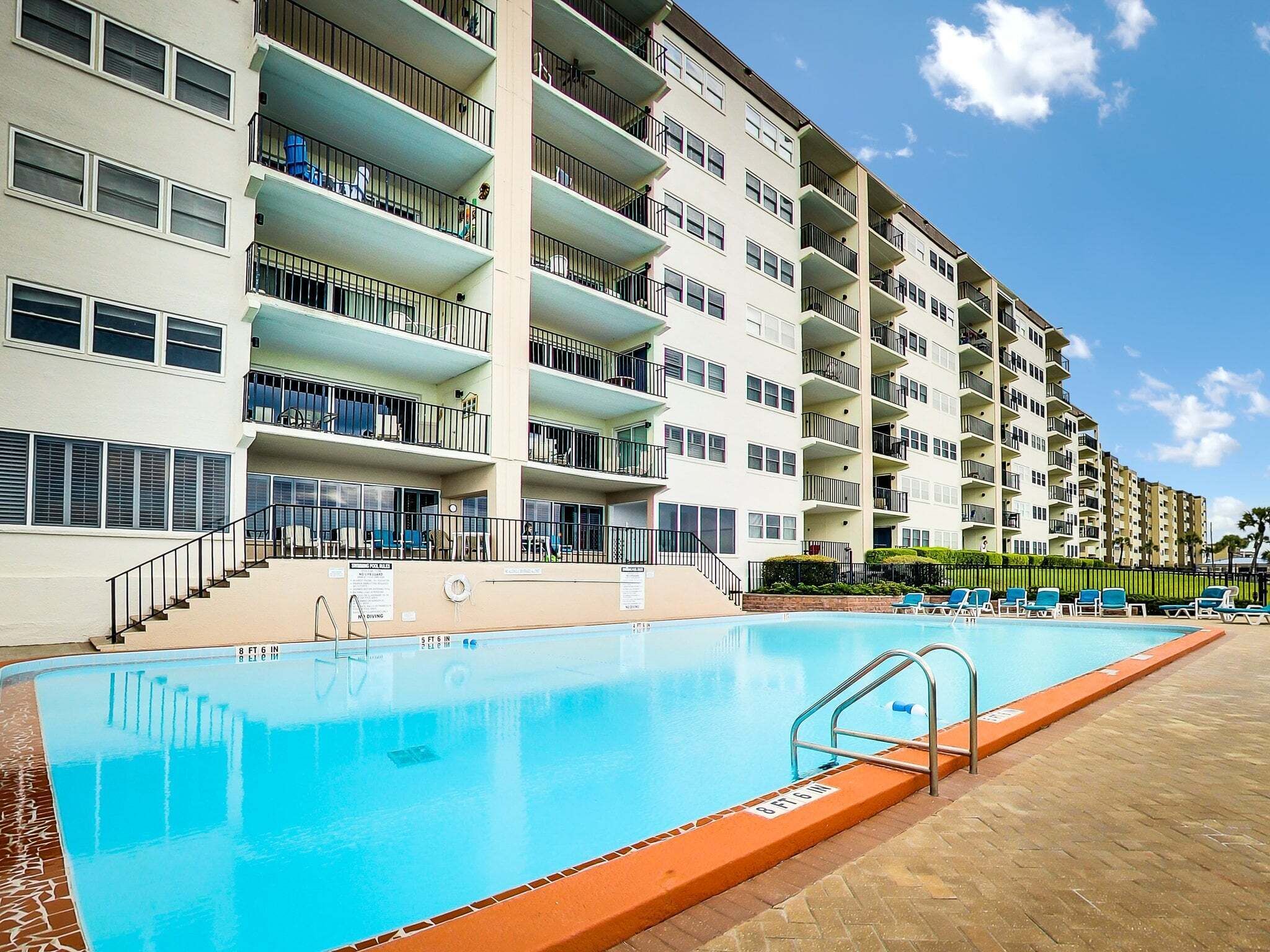 Een meerhoog hotel met een zwembad, terras en heldere lucht.