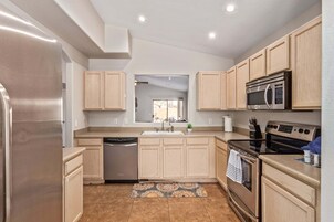 A modern kitchen with light wood cabinets, stainless steel appliances, and a central island.