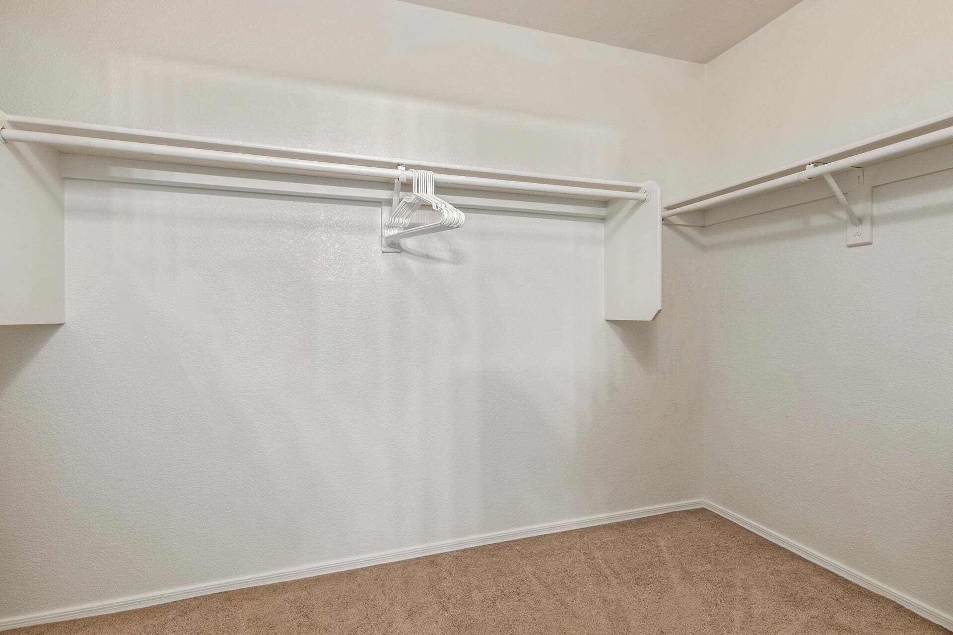 Une pièce aux murs blancs, avec un tapis beige et deux tringles à vêtements blanches.