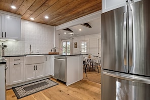A kitchen with white cabinets, a stainless steel refrigerator, wooden ceiling, and a dining area with a table and chairs. - Happy Hiker (Highlands)