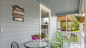 Eine Veranda mit Tisch und Stühlen, ein Willkommen-Schild und Blick auf das Haus.