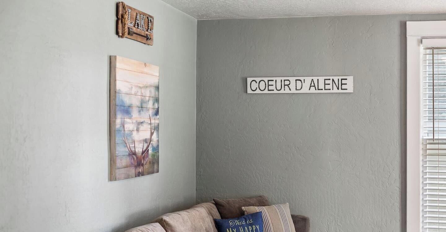 Quarto com parede cinza, quadro emoldurado de um veado e placa com a inscrição "COEUR D'ALENE".
