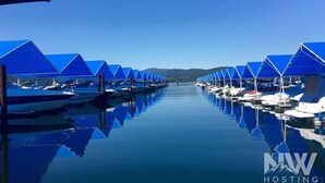 Ein Yachthafen mit vertäuten Booten unter blauen Markisen, ruhiges Wasser spiegelt die Boote und Markisen wider, und ein klarer Himmel.