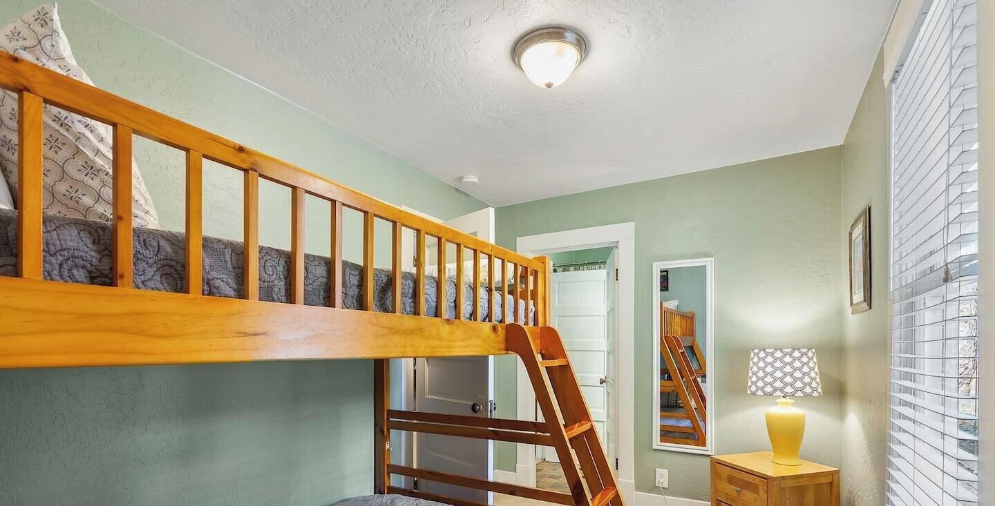 A bunk bed with a wooden ladder, a bedside table with a lamp, and a door in the background.