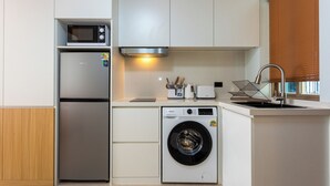 Eine kleine Küche mit Kühlschrank, Mikrowelle, Waschmaschine und Spüle mit Wasserhahn.