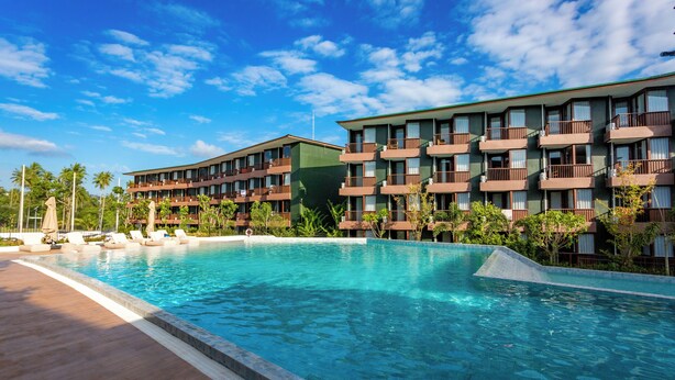 Ein Hotel mit Schwimmbad, mehreren Balkonen und einem Garten in tropischer Gestaltung.
