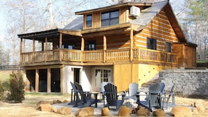 A log cabin with a balcony, outdoor seating, and a stone wall. - Karaoke, Hot Tub, 1GB Wifi - The Rock House - LUX (Rogers)