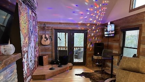 A cozy living room with a fireplace, a guitar, a television, and a comfortable seating area. - Karaoke, Hot Tub, 1GB Wifi - The Rock House - LUX (Rogers)