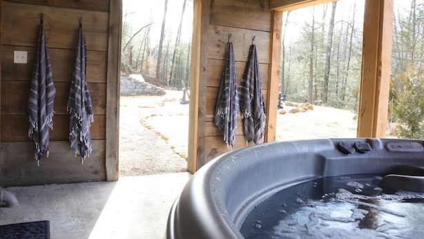 A wooden cabin with a hot tub, wooden walls, and a view of a forest. - Karaoke, Hot Tub, 1GB Wifi - The Rock House - LUX (Rogers)