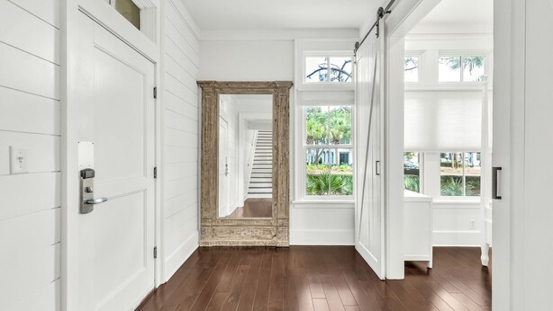 Un couloir avec des portes blanches, un plancher en bois et une vue sur un escalier menant à un balcon.