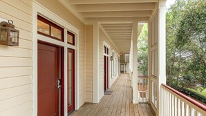 Une véranda couverte avec un plancher en bois, des portes rouges et une balustrade blanche.