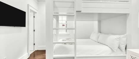 Habitación con literas, ropa de cama blanca y un televisor fijado a la pared.