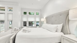 Une chambre d’hôtel moderne avec un grand lit, une tête de lit, des tables de chevet et une vue sur l’extérieur grâce à de grandes fenêtres.