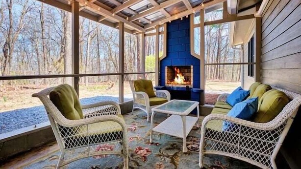 A covered outdoor seating area with wicker furniture, a fire pit, and a view of the surrounding trees. - The Pink Lady (Highlands)