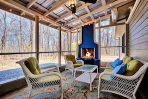 A covered outdoor seating area with wicker furniture, a fire pit, and a view of the surrounding trees. - The Pink Lady (Highlands)