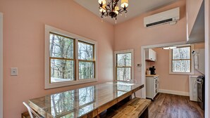 A kitchen with a long wooden table, white cabinets, and a view of trees through the windows. - The Pink Lady (Highlands)