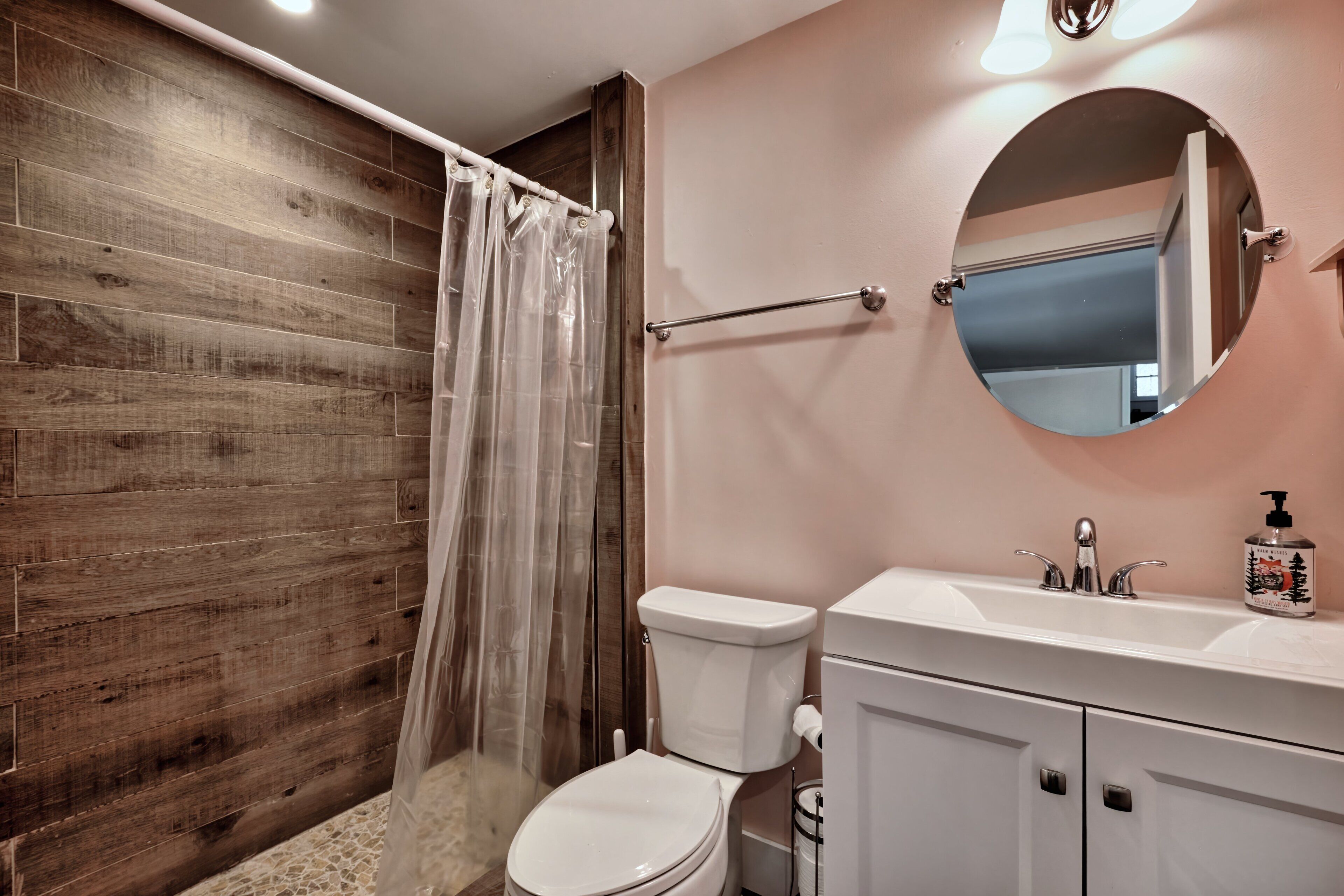 Ein Badezimmer mit Holzwand, Duschvorhang, Toilette, Waschbecken, Spiegel und Seifenspender.