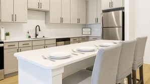 A modern kitchen with white cabinetry, a stainless steel refrigerator, and a central island with seating. - Gym, Pool, Washerdryer, Workerfriendly A+location (Sherman)
