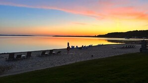 A beach with lounge chairs and a calm body of water during sunset. - Walkout Beachfront Condo: Pointes North Resort 106 (Traverse City)
