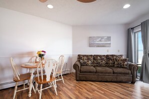 A living room with a brown sofa, wooden chairs, a dining table with a vase of flowers, and a painting on the wall. - Walkout Beachfront Condo: Pointes North Resort 106 (Traverse City)